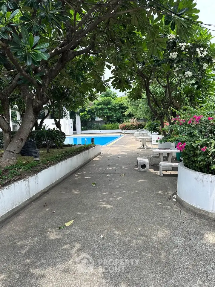 Serene garden pathway leading to a refreshing pool surrounded by lush greenery.
