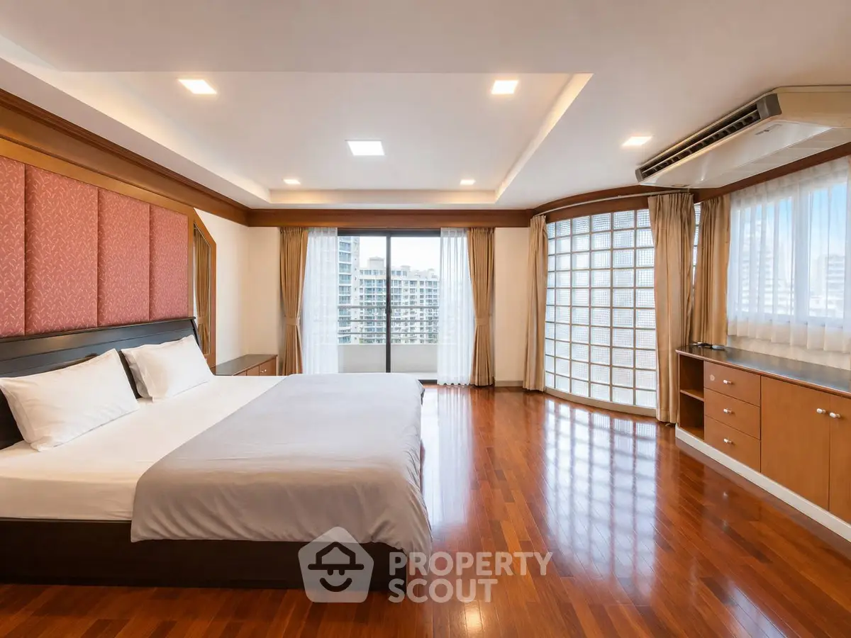 Spacious bedroom with hardwood floors and city view, featuring modern design and ample natural light.