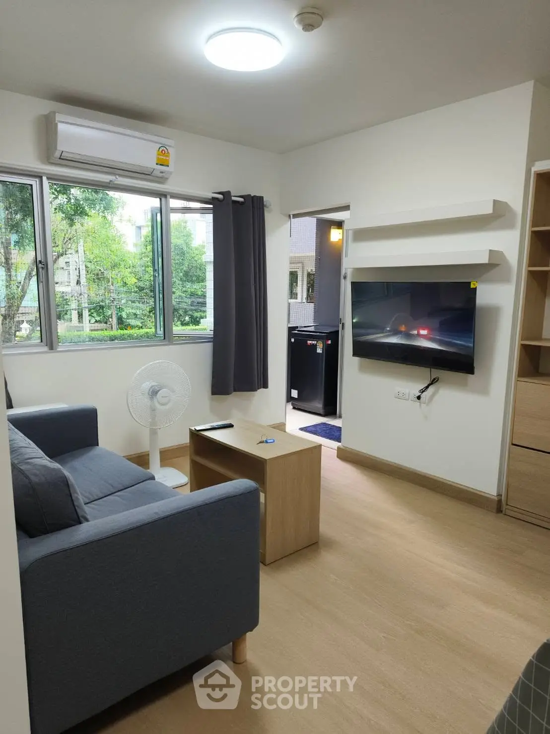 Modern living room with sleek furniture and wall-mounted TV, featuring large windows and natural light.