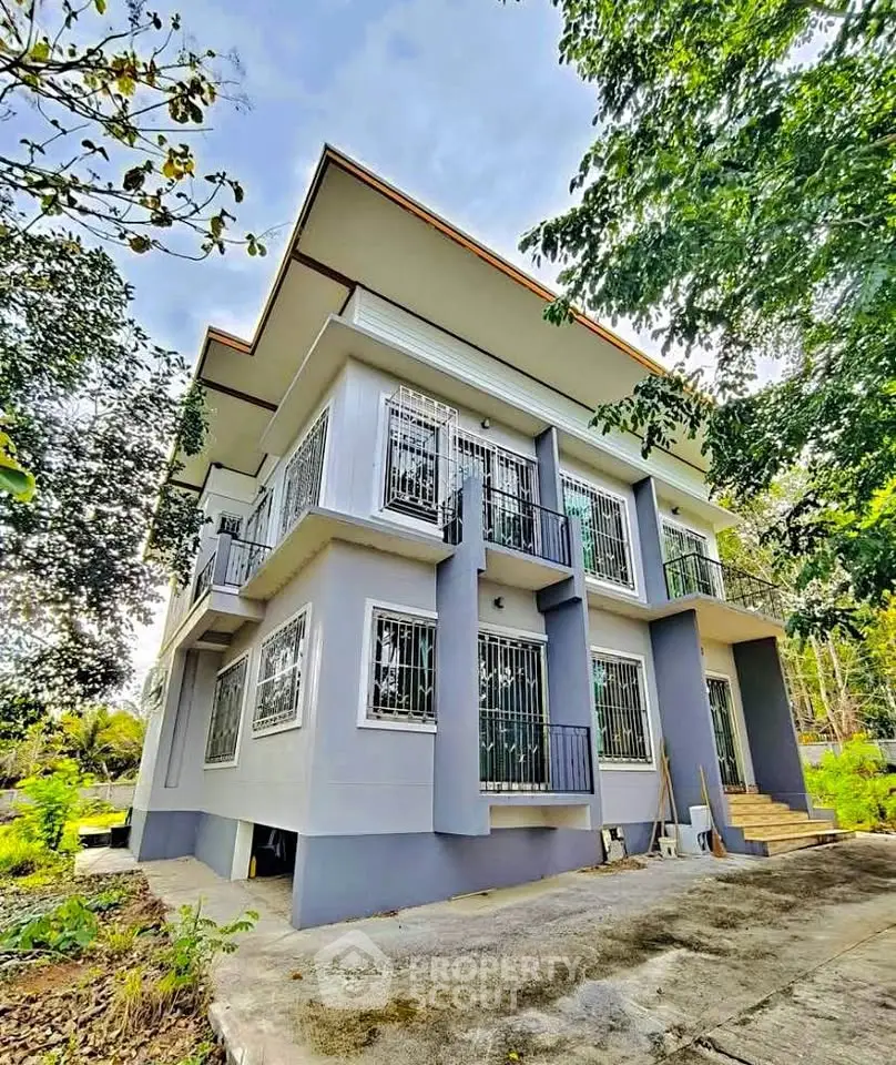 Modern two-story house with large windows and lush greenery surroundings.