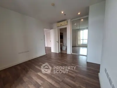 Spacious empty bedroom with wooden flooring and mirrored closet doors.
