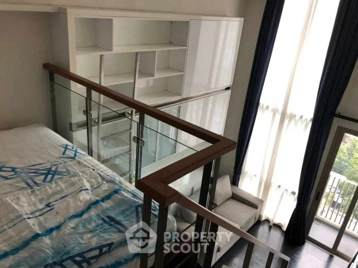 Modern loft bedroom with high ceilings and large windows, featuring a stylish glass railing and built-in shelving.