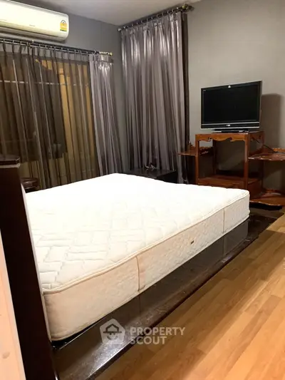 Cozy bedroom with elegant curtains and wooden flooring, featuring a comfortable mattress and TV setup.