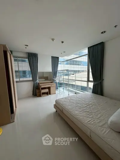 Spacious bedroom with modern furnishings and large windows offering city views.