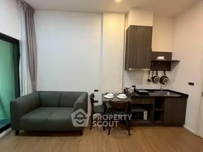 Modern compact living room with kitchenette, featuring sleek cabinetry and cozy seating.