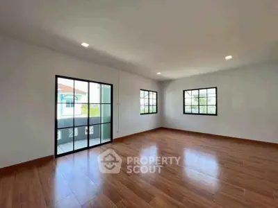 Spacious empty living room with wooden flooring and large windows in modern home.