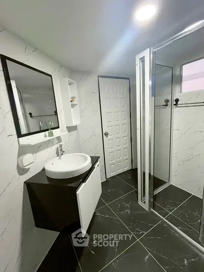 Modern bathroom with sleek black and white design, featuring a glass shower and stylish vanity.