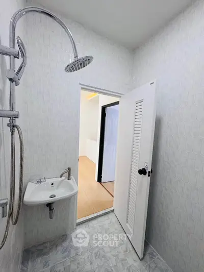 Modern bathroom with shower and sink, featuring sleek white tiles and open door to adjacent room.