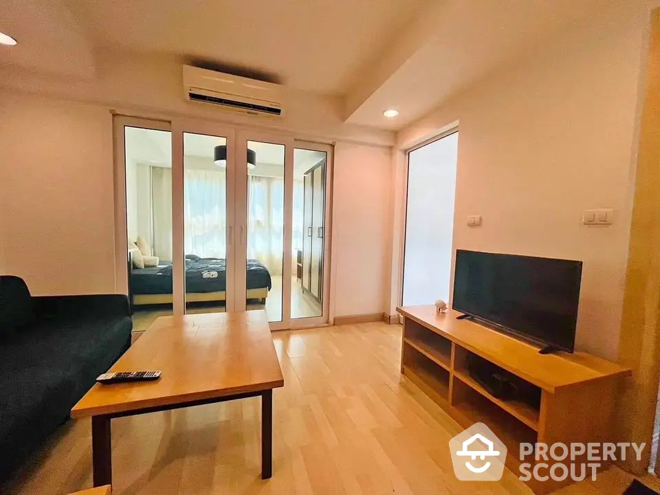 Modern living room with wooden flooring and sliding glass doors leading to a cozy bedroom.