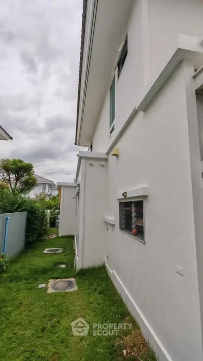 Modern white exterior of a residential building with lush green lawn and overcast sky.