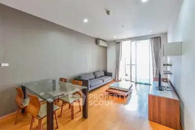 Modern living room with wooden flooring, glass dining table, and cozy sofa near large window.