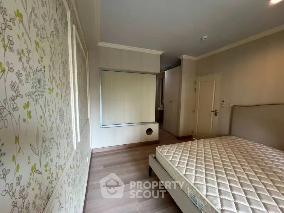 Spacious bedroom with elegant wallpaper and hardwood flooring, featuring a comfortable bed and ample natural light.