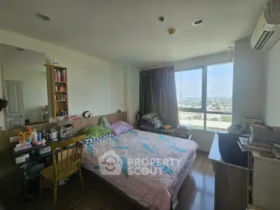 Cozy bedroom with large window offering city views, featuring a comfortable bed and ample storage space.