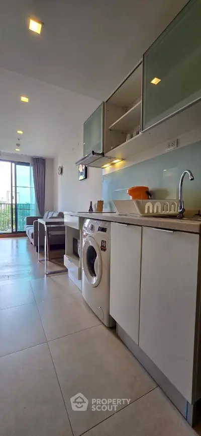 Modern open-plan living room with kitchen and washing machine, bright and airy space.