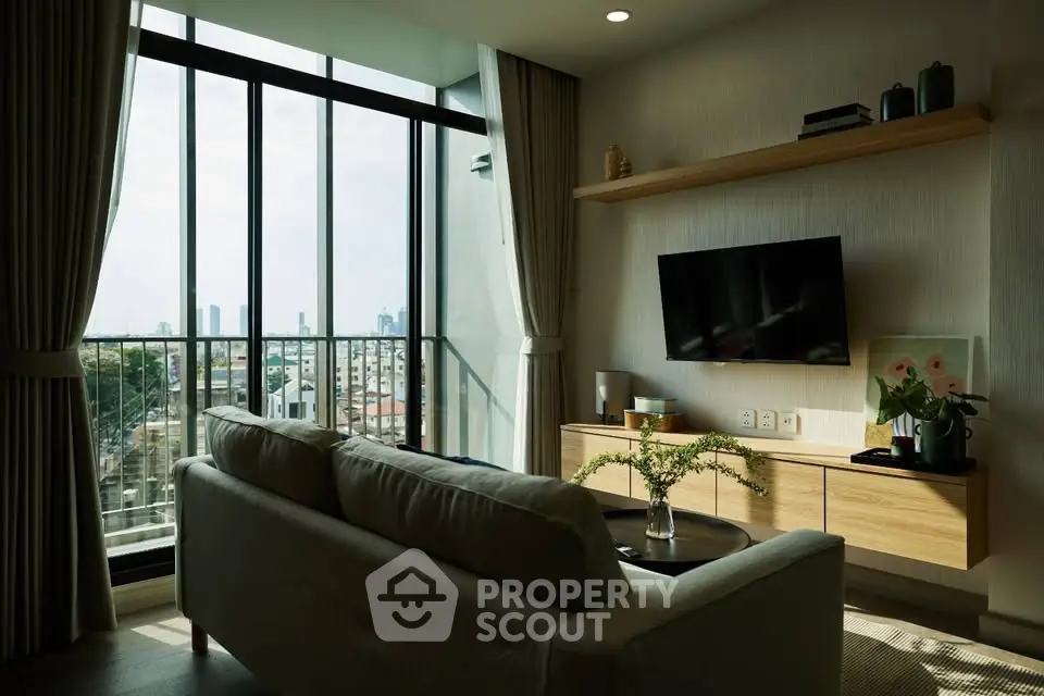 Modern living room with large windows offering city skyline view, featuring cozy sofa and wall-mounted TV.