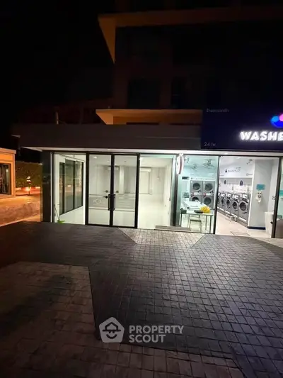 Modern laundromat exterior with glass doors and bright interior lighting at night.