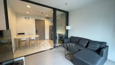 Modern living room with sleek furniture and glass partition leading to dining area in a stylish apartment.