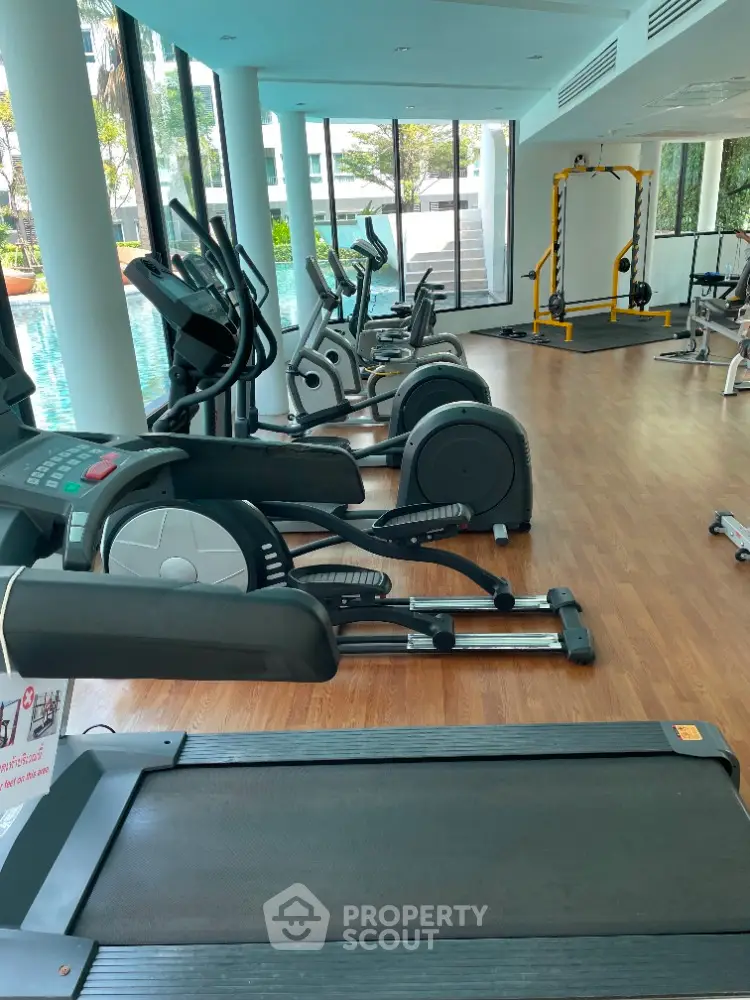 Modern gym with state-of-the-art equipment and pool view in luxury residential complex.