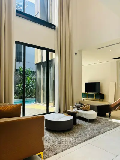 Luxurious living room with high ceilings and pool view, featuring modern furniture and elegant decor.