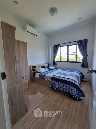 Cozy bedroom with wooden furniture and large window offering natural light.