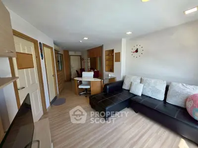 Modern living room with sleek black sofa and wall clock, featuring open layout and wooden flooring.