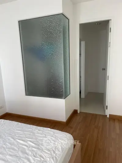 Modern bedroom with wooden flooring and frosted glass feature wall