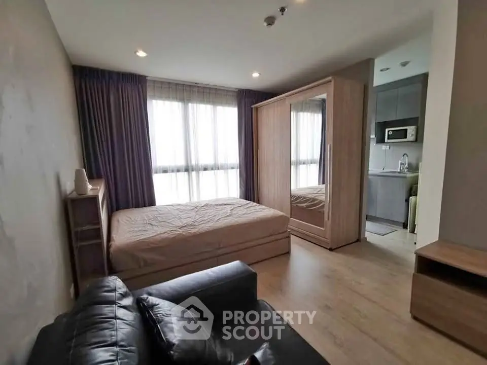 Modern studio apartment with cozy bedroom and compact kitchen area, featuring sleek furnishings and natural light.