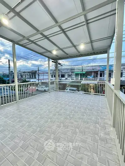 Spacious covered balcony with tiled flooring and scenic neighborhood view.