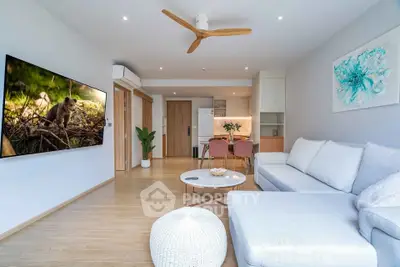 Modern living room with large TV, stylish furniture, and open kitchen layout