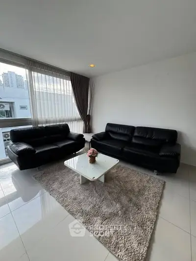 Modern living room with sleek black sofas and city view window.