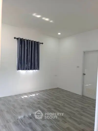 Spacious empty room with modern flooring and window curtains, ideal for customization.