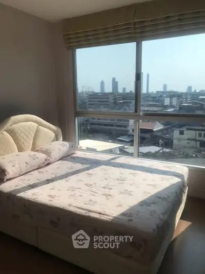 Cozy bedroom with large window offering stunning city skyline view, perfect for urban living.
