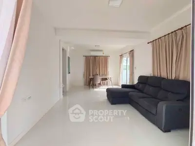 Spacious living room with modern sofa and dining area, featuring large windows and elegant curtains.