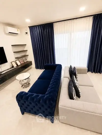 Elegant living room with plush blue and gray sofas, modern decor, and large window with curtains.