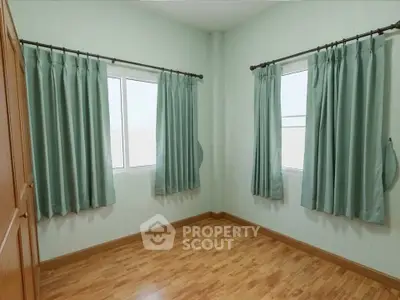 Spacious bedroom with wooden flooring and large windows for natural light.