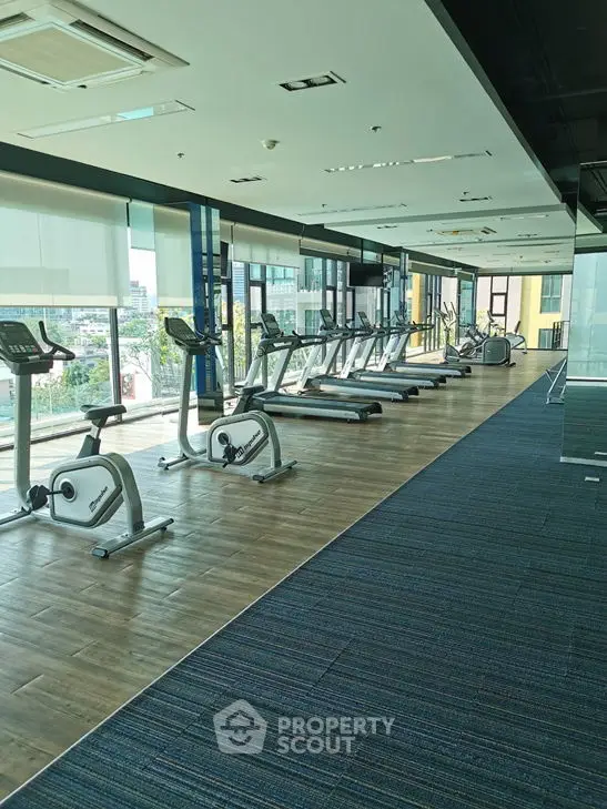 Spacious modern gym with exercise equipment and large windows offering city views.