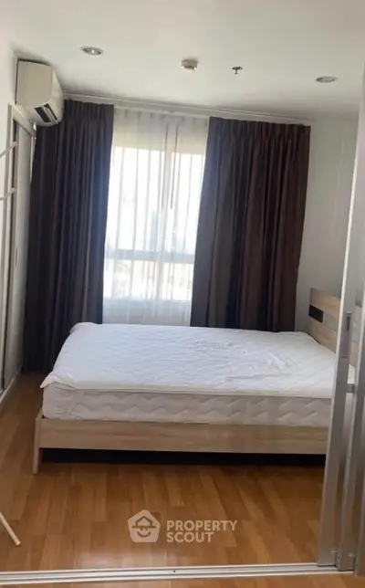 Cozy bedroom with wooden flooring and large window, featuring a comfortable bed and air conditioning.