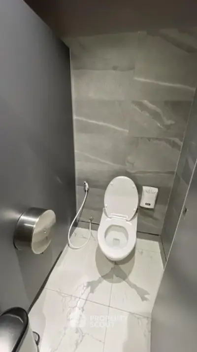 Modern bathroom with sleek gray tiles and white fixtures, featuring a toilet and bidet spray.