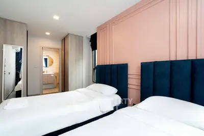 Modern bedroom with twin beds and stylish decor, featuring a glimpse of an ensuite bathroom.