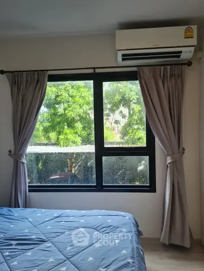 Cozy bedroom with large window and lush green view, featuring modern air conditioning.