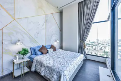 Luxurious bedroom with floor-to-ceiling windows offering stunning city views, elegant decor, and modern furnishings.
