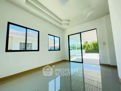 Bright and spacious living room with large windows and sliding glass door opening to a sunny patio.