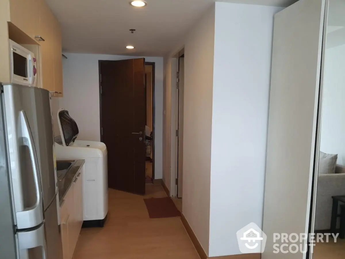 Modern apartment hallway with kitchen and washing machine, featuring sleek appliances and wooden flooring.