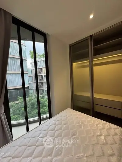 Modern bedroom with large window and built-in closet, offering a serene view of greenery.