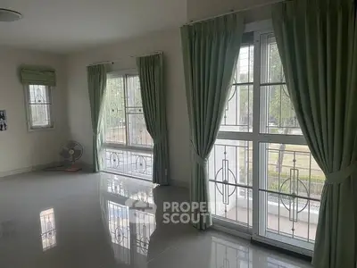 Spacious living room with large windows and green curtains, perfect for natural light lovers.