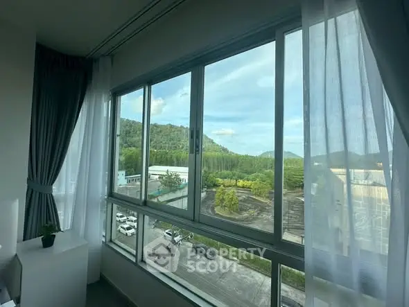 Stunning view from a modern apartment window overlooking lush greenery and hills.