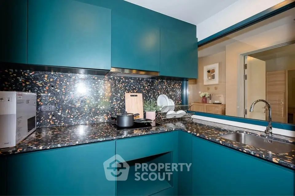 Modern kitchen with teal cabinets and terrazzo countertops, featuring sleek design and open layout.