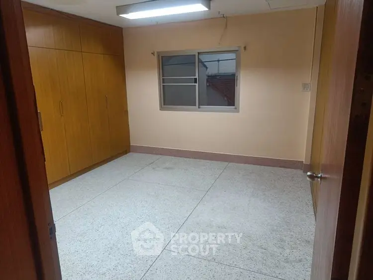 Spacious empty room with built-in wooden wardrobe and window view.