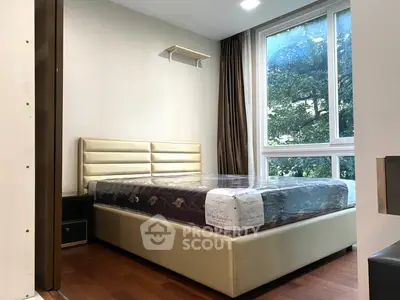 Modern bedroom with large window and elegant bed frame, showcasing natural light and hardwood floors.
