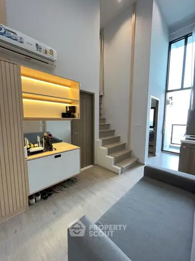 Modern duplex interior with stylish staircase and cozy living area, featuring sleek storage solutions and high ceilings.